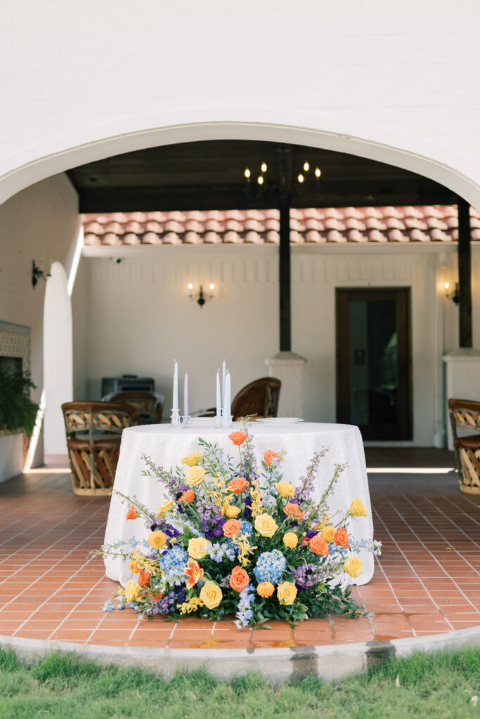 Large, vibrant ground floral arrangement positioned in front of the sweetheart table, designed by Kendra’s Events.